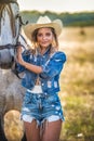 Beautiful blonde woman with curly hair with white hat and horse. Portrait of a girl with denim and her horse Royalty Free Stock Photo