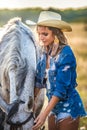 Beautiful blonde woman with curly hair with white hat and horse. Portrait of a girl with denim and her horse Royalty Free Stock Photo