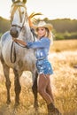 Beautiful blonde woman with curly hair with white hat and horse. Portrait of a girl with denim and her horse. Royalty Free Stock Photo