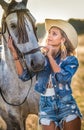 Beautiful blonde woman with curly hair with white hat and horse. Portrait of a girl with denim and her horse Royalty Free Stock Photo