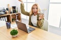 Beautiful blonde woman doing online shopping holding supermarket cart at the office celebrating victory with happy smile and Royalty Free Stock Photo