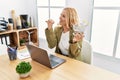 Beautiful blonde woman doing online shopping holding supermarket cart at the office pointing thumb up to the side smiling happy Royalty Free Stock Photo