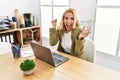 Beautiful blonde woman doing online shopping holding supermarket cart at the office screaming proud, celebrating victory and Royalty Free Stock Photo