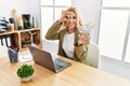 Beautiful blonde woman doing online shopping holding supermarket cart at the office smiling happy doing ok sign with hand on eye Royalty Free Stock Photo