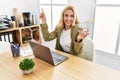 Beautiful blonde woman doing online shopping holding supermarket cart at the office smiling happy pointing with hand and finger to Royalty Free Stock Photo