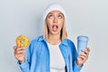 Beautiful blonde woman eating doughnut and drinking coffee angry and mad screaming frustrated and furious, shouting with anger Royalty Free Stock Photo