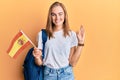 Beautiful blonde woman exchange student holding spanish flag doing ok sign with fingers, smiling friendly gesturing excellent
