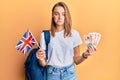 Beautiful blonde woman exchange student holding uk flag and pounds depressed and worry for distress, crying angry and afraid