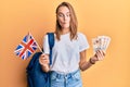 Beautiful blonde woman exchange student holding uk flag and pounds making fish face with mouth and squinting eyes, crazy and