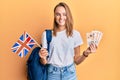 Beautiful blonde woman exchange student holding uk flag and pounds smiling with a happy and cool smile on face