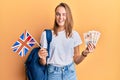 Beautiful blonde woman exchange student holding uk flag and pounds winking looking at the camera with sexy expression, cheerful