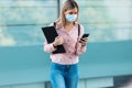 Beautiful blonde woman in face mask using her mobile phone while walking in the street Royalty Free Stock Photo