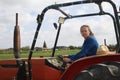 Beautiful blonde woman farmer riding a red tractor to till the soil in order to be able to work in the vegetable garden