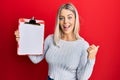 Beautiful blonde woman holding clipboard with blank space pointing thumb up to the side smiling happy with open mouth Royalty Free Stock Photo