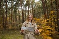 Beautiful happy woman holding mobile phone using map to navigate in autumn forest. Happy tourist trying to find best way Royalty Free Stock Photo