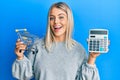 Beautiful blonde woman holding small supermarket shopping cart and calculator smiling and laughing hard out loud because funny