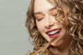 Beautiful blonde woman with long curly hair laughing on gray background, cute face close up Royalty Free Stock Photo