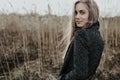 Pretty and young woman with long blonde hair dressed in wool coat looking at camera over her shoulder and smiling. Background bulr Royalty Free Stock Photo