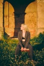 Beautiful blonde woman in an office suit sitting on a chair in nature on the background of an old castle. Royalty Free Stock Photo