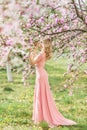 Beautiful blonde woman in a pink long dress in a spring blooming garden Royalty Free Stock Photo