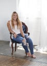 Beautiful blonde woman poses with vintage chair in white tank and jeans Royalty Free Stock Photo