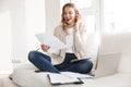 Beautiful blonde woman posing sitting indoors at home using laptop computer talking by mobile phone Royalty Free Stock Photo