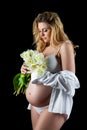 Beautiful blonde woman with a pregnant tummy wearing a white shirt and holding flowers white tulips in her hands. Girl posing on a Royalty Free Stock Photo