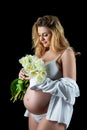 Beautiful blonde woman with a pregnant tummy wearing a white shirt and holding flowers white tulips in her hands. Girl posing on a Royalty Free Stock Photo