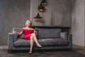 beautiful blonde woman in red dress sitting on sofa Royalty Free Stock Photo