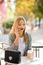 Beautiful blonde woman with red lips, sits at a table in a street cafe, talking on the phone Royalty Free Stock Photo