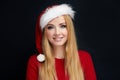 Beautiful blonde woman in Santa Claus hat looking at camera against black wall Royalty Free Stock Photo