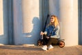 Beautiful blonde woman on scooter near grey columns at sunset holds a water bottle on hand Royalty Free Stock Photo