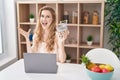 Beautiful blonde woman shopping online with laptop celebrating victory with happy smile and winner expression with raised hands Royalty Free Stock Photo