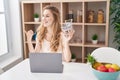 Beautiful blonde woman shopping online with laptop pointing thumb up to the side smiling happy with open mouth Royalty Free Stock Photo