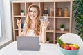 Beautiful blonde woman shopping online with laptop smiling happy pointing with hand and finger to the side Royalty Free Stock Photo
