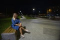 A beautiful blonde woman sits in a park on a late summer evening. A woman relaxes on a bench in a city park after work