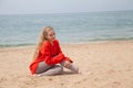 Beautiful blonde woman sits on the sand on an empty beach by the sea Royalty Free Stock Photo