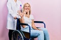 Beautiful blonde woman sitting on wheelchair with collar neck showing and pointing up with fingers number five while smiling