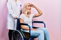 Beautiful blonde woman sitting on wheelchair with collar neck very happy and smiling looking far away with hand over head Royalty Free Stock Photo
