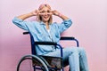 Beautiful blonde woman sitting on wheelchair doing peace symbol with fingers over face, smiling cheerful showing victory Royalty Free Stock Photo