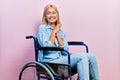 Beautiful blonde woman sitting on wheelchair laughing nervous and excited with hands on chin looking to the side Royalty Free Stock Photo