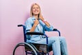 Beautiful blonde woman sitting on wheelchair very happy and excited doing winner gesture with arms raised, smiling and screaming Royalty Free Stock Photo