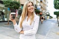 Beautiful blonde woman smiling happy outdoors on a sunny day drinking a take away cup of coffee Royalty Free Stock Photo