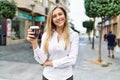 Beautiful blonde woman smiling happy outdoors on a sunny day drinking a take away cup of coffee Royalty Free Stock Photo