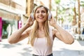 Beautiful blonde woman smiling happy outdoors on a sunny day wearing headphones listening to music Royalty Free Stock Photo