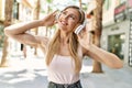 Beautiful blonde woman smiling happy outdoors on a sunny day wearing headphones listening to music Royalty Free Stock Photo