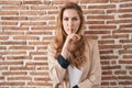 Beautiful blonde woman standing over bricks wall asking to be quiet with finger on lips Royalty Free Stock Photo