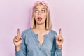 Beautiful blonde woman standing over pink background amazed and surprised looking up and pointing with fingers and raised arms Royalty Free Stock Photo