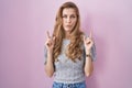 Beautiful blonde woman standing over pink background pointing up looking sad and upset, indicating direction with fingers, unhappy Royalty Free Stock Photo