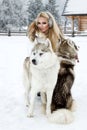 Beautiful blonde woman, standing on snow and holding Husky dogs view of mountains and snow.